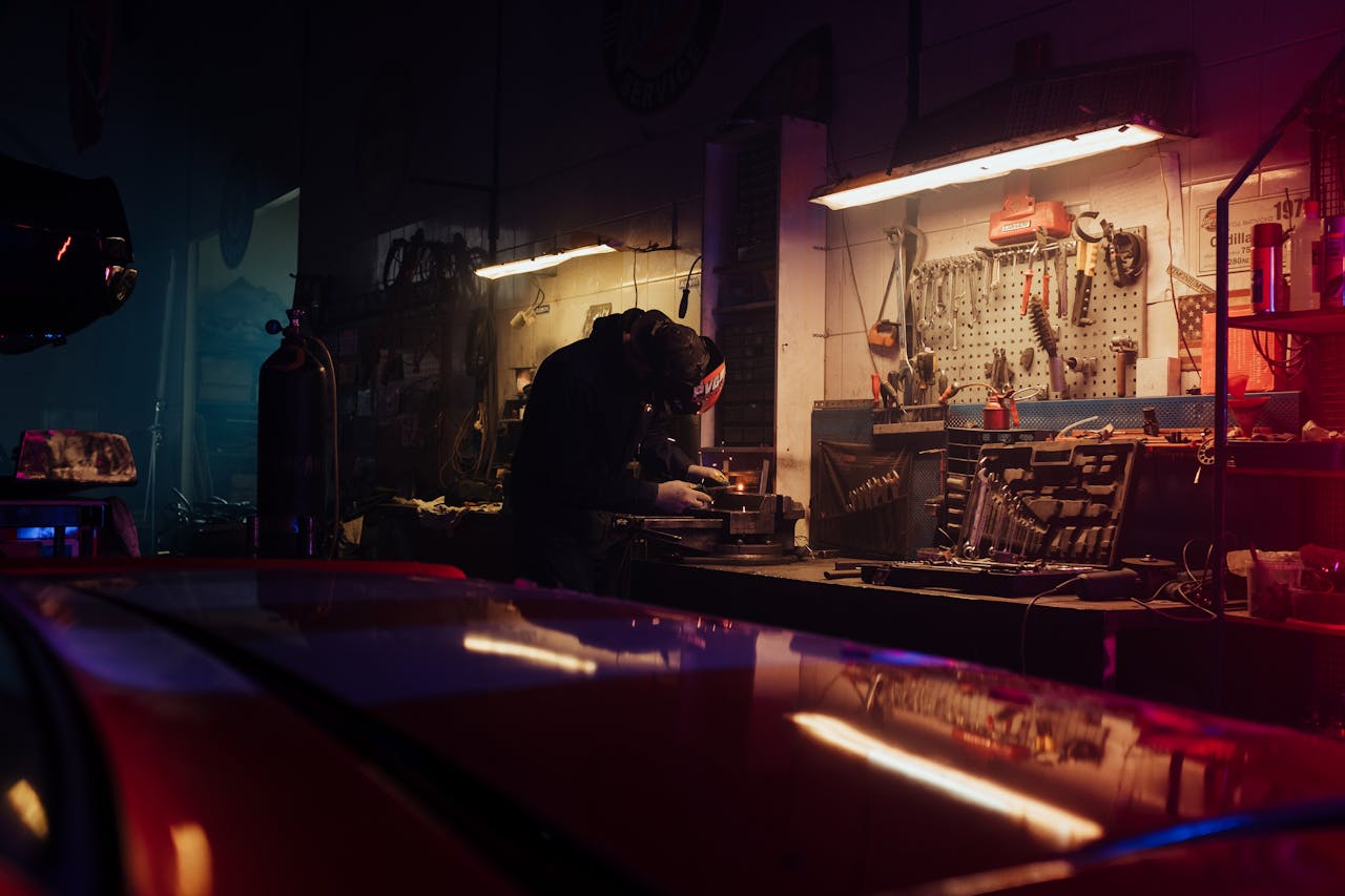 A mechanic diligently working on a car part in a tool-filled garage.